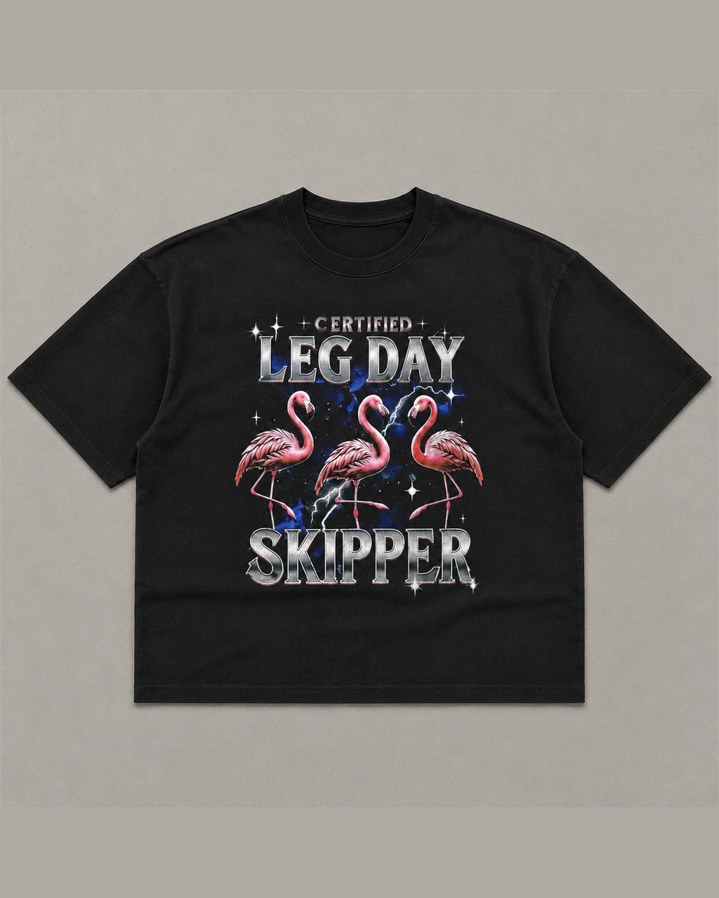Black heavyweight tee reading CERTIFIED LEG DAY SKIPPER in chrome lettering above three pink flamingos on a blue lightning background