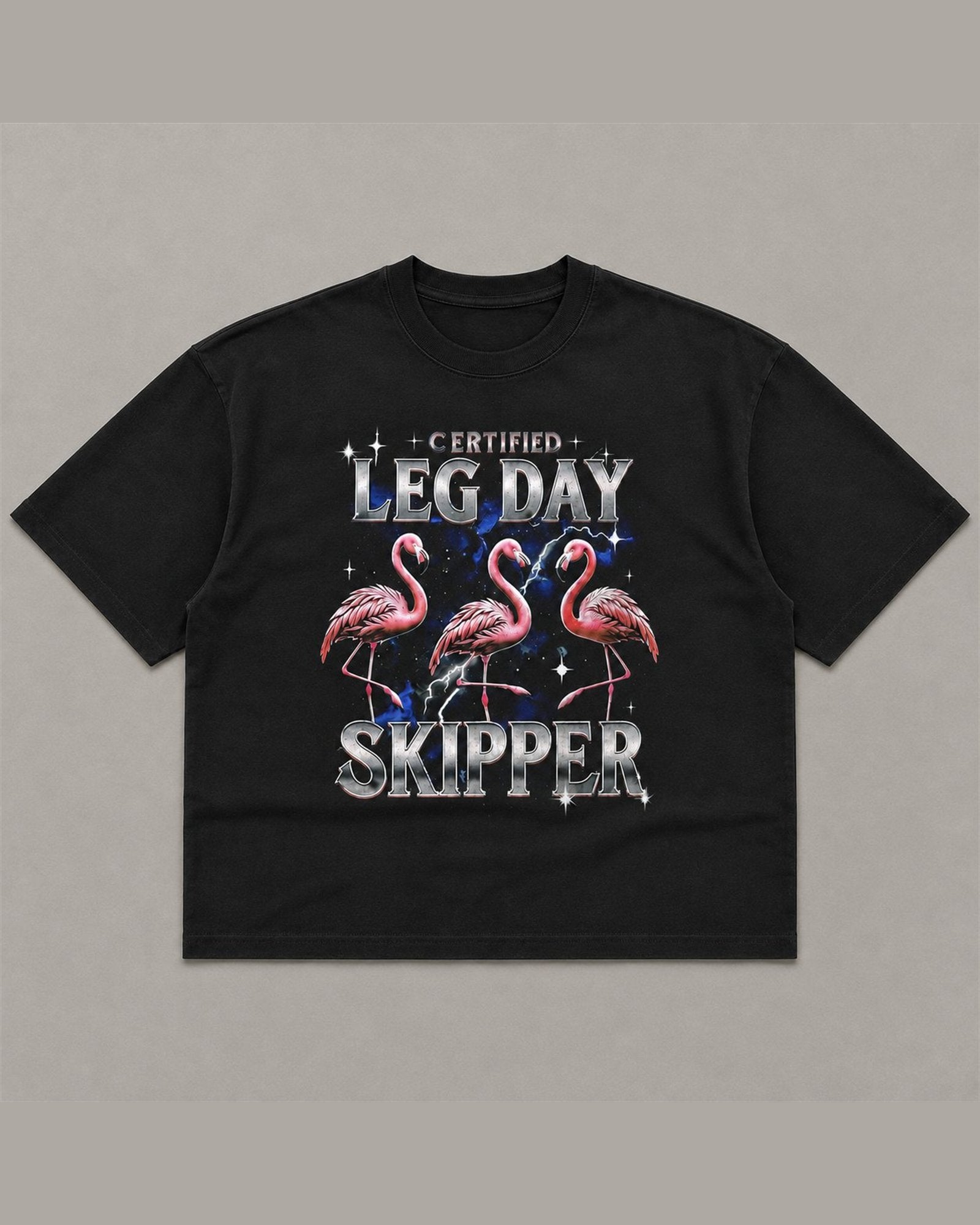Black heavyweight tee reading CERTIFIED LEG DAY SKIPPER in chrome lettering above three pink flamingos on a blue lightning background