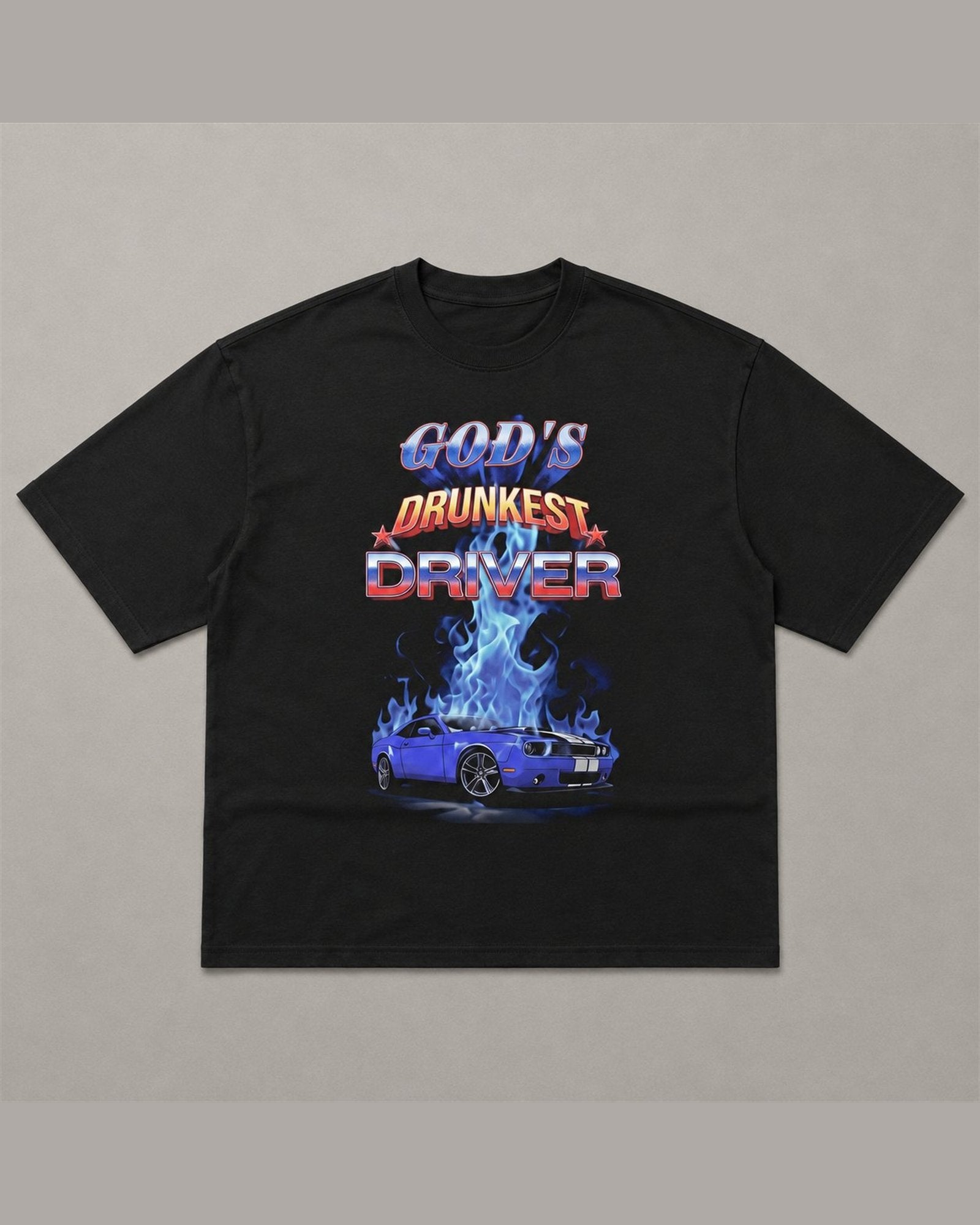 Black heavyweight tee reading GOD'S DRUNKEST DRIVER in chrome and flame lettering above a blue muscle car surrounded by blue fire